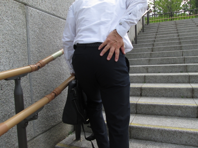 腰の痛みを感じながら階段を歩く男性の写真